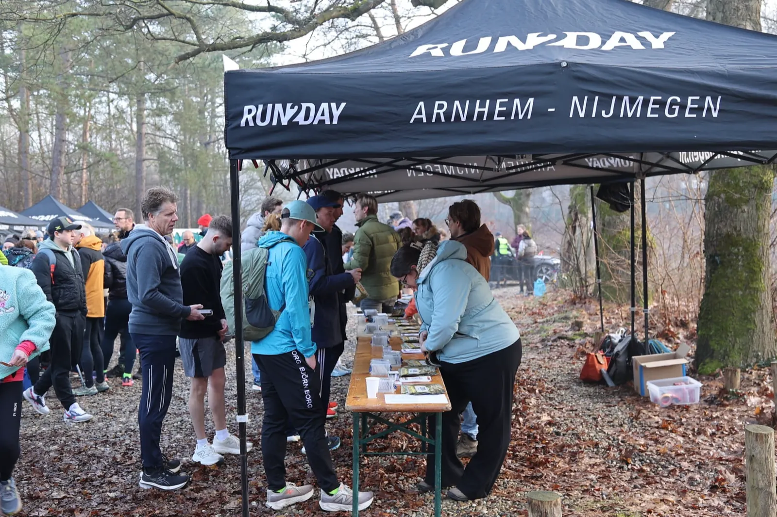 Vrijwilligers en lopers rond de tent in het bos